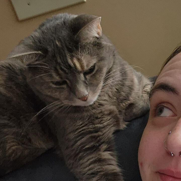 A woman sits with a white golden doodle in her lap and smiles.